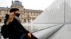 Женщина в маске сидит перед Лувром в Париже