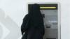 Женщина в абайе вынимает деньги из банкомата
