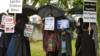 Протестующие держат плакаты и плакаты во время своей первой демонстрации после того, как судебный запрет запретил проведение акций сразу за пределами начальной школы Андертон-Парк