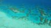 Вид с воздуха на Большой Барьерный риф. Глубокая синяя вода вдали и светло-голубая на мелководье на переднем плане. Коралловые узоры посередине.