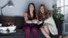 Две молодые женщины с веселым выражением лица играют на диване в видеоигры