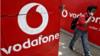 Мужчина разговаривает по мобильному телефону, проходя мимо логотипов Vodafone, нарисованных на придорожной стене в Калькутте 20 мая 2014 г.