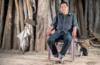 Чагаби Этакоре сидит в кресле в лесу с кошкой рядом с ним