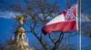 Купол Капитолия штата Миссисипи виден вдалеке, пока развевается флаг штата Миссисипи