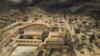 На рисунке показан вид Помпеи с высоты птичьего полета с его амфитеатром и римскими постройками, когда густое черное облако спускается на город сверху кадра.