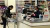 Кассир супермаркета Tesco в защитной маске и перчатках помогает покупателю за пластиковым экраном