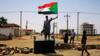 Суданский протестующий держит национальный флаг, стоит на баррикаде вдоль улицы, требуя, чтобы Переходный военный совет страны передал власть гражданским лицам, в Хартуме, Судан, 5 июня 2019 г.