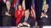 Президент США Джордж Буш закрывает ручку после подписания Североамериканского соглашения о свободной торговле в штаб-квартире Организации американских государств 17 декабря 1992 года в Вашингтоне, округ Колумбия. Смотрят посол Мексики Густаво Петричиоли (слева), торговый представитель США Карла Хиллз и посол Канады. Дерек Бёрни (R)