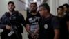 Рожерио Авелино да Силва, также известный как Рожерио 157, которого власти обвиняют в том, что он является начальником наркобизнеса в трущобах Росинья, сопровождают полицейские в комплексе полицейского участка в Рио-де-Жанейро, Бразилия, 6 декабря 2017 года.