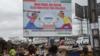 Люди проходят мимо рекламного щита в Йопугоне, популярном районе Абиджана, который способствует мирным выборам в Кот-д'Ивуаре
