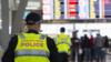 Офицер полиции в желтом флюоресцентном жилете стоит перед экраном вылета в аэропорту Сиднея