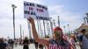 Мужчина держит табличку во время демонстрации в Калифорнии в начале мая с надписью «Фейковые новости - это настоящий вирус»