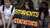 Трое студентов сидят на обочине улицы с плакатом протеста: «Студенты, а не статистика»
