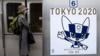 Пассажир в маске стоит рядом с плакатом с олимпийским талисманом Токио-2020 Мираитовой в поезде в Токио 20 апреля 2020 г.