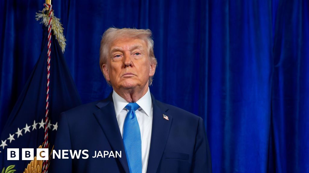 青い幕を背に、紺のスーツに水色のネクタイをしたトランプ大統領が前を見ている