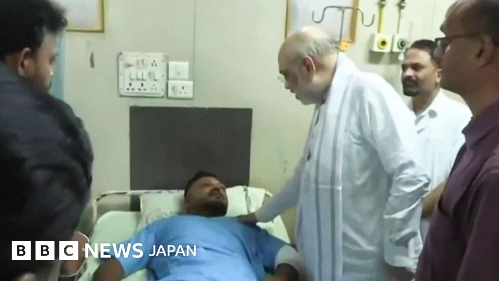 病院のベッドに横たわる男性を、複数人が囲んで見舞っている