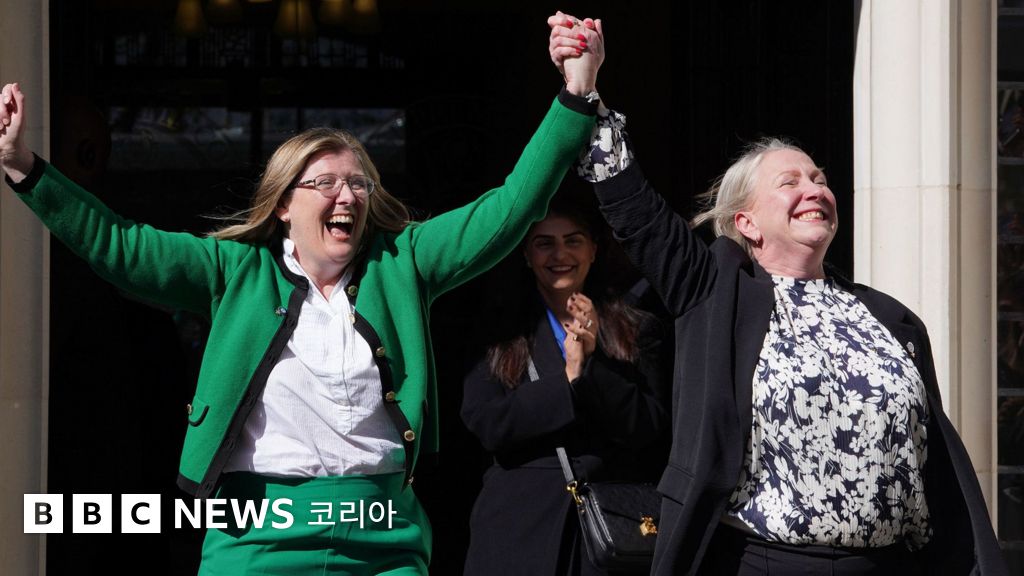 Two women hold hands in the air in celebration in a doorway