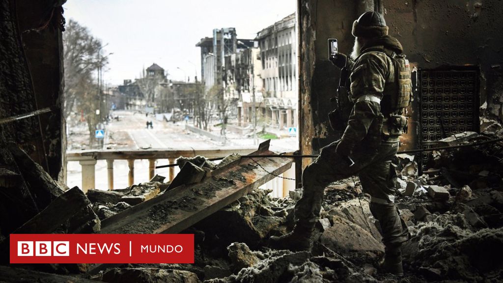 Un hombre con uniforme militar se para en un edificio destruido