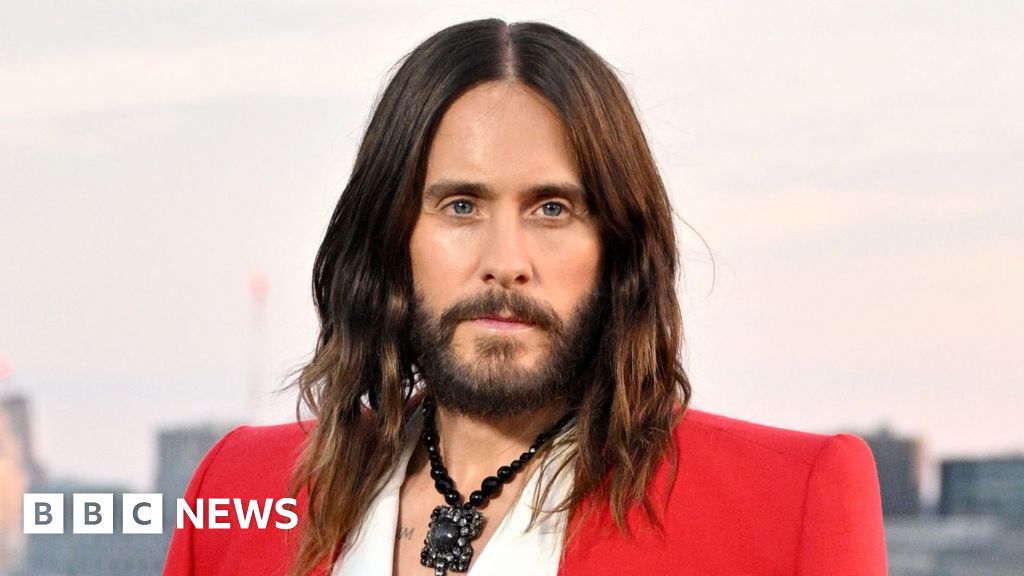 Jared Leto en un evento público, con un fondo oscuro, mirando hacia un lado. Su cabello es oscuro y lleva una chaqueta elegante. La imagen acompaña una noticia sobre acusaciones de conducta sexual.
