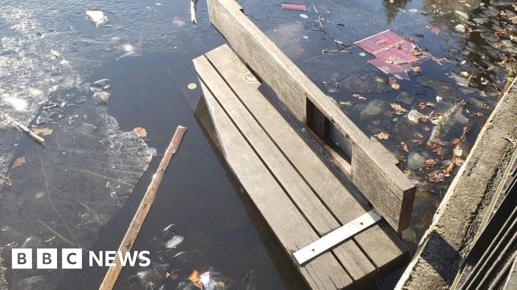 The remains of a broken wooden bench floating on the surface of a body of water surrounded by pieces of broken ice. 