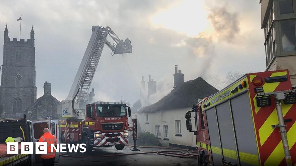 Multiple fire crews are pictured in the village. One fire engine is positioned on support stilts while a ladder extends from the rear of the vehicle so firefighters can squirt water over the thatched-roofed cottages. 