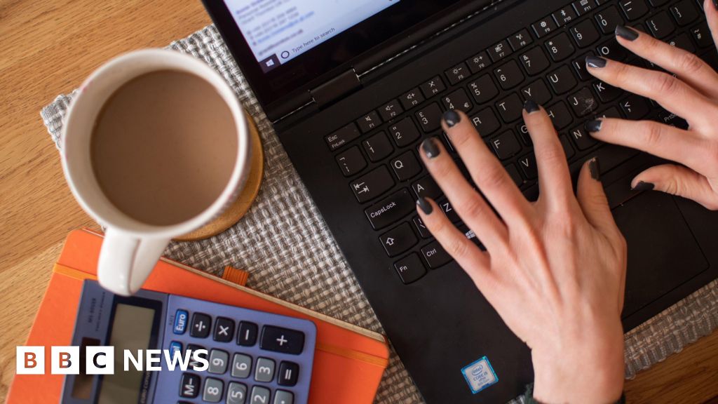 Generic of person typing on laptop with calculator and cup of tea