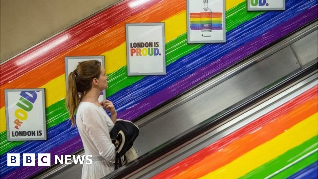 People ride a tube escalator decorated with the Pride flag colours