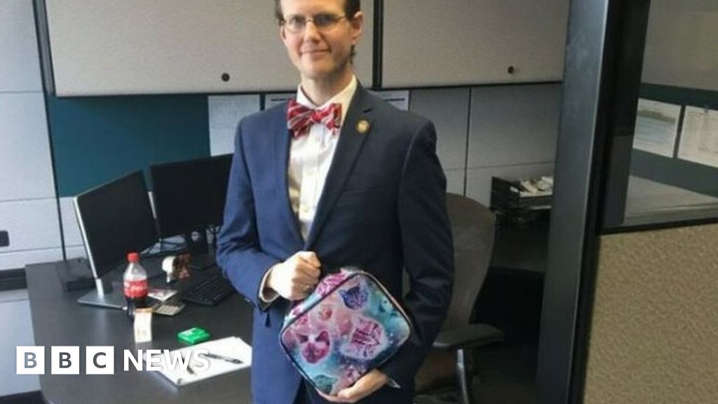 photo shows David Pendragon wearing a suit in an office and holding a lunchbox with pictures of cats on it.