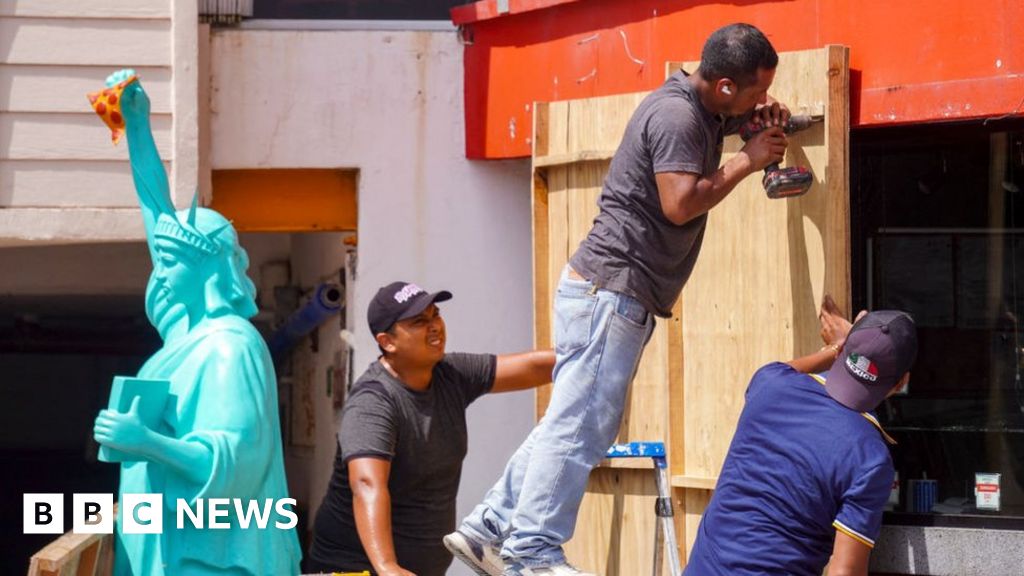 Workers nail wooden boards to the outside of a building in Mexico, ahead of the arrival of Hurricane Milton on 7 October 2024