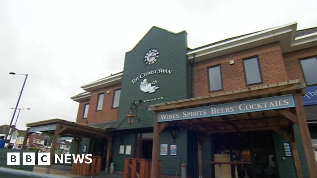 External shot of a brick-built pub with a large green panel featuring a clock and The Clumsy Swan pub sign