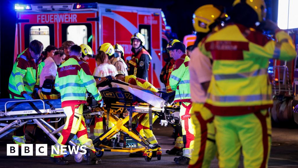 A number of emergency services personnel standing near an ambulance, with a person on a stretcher