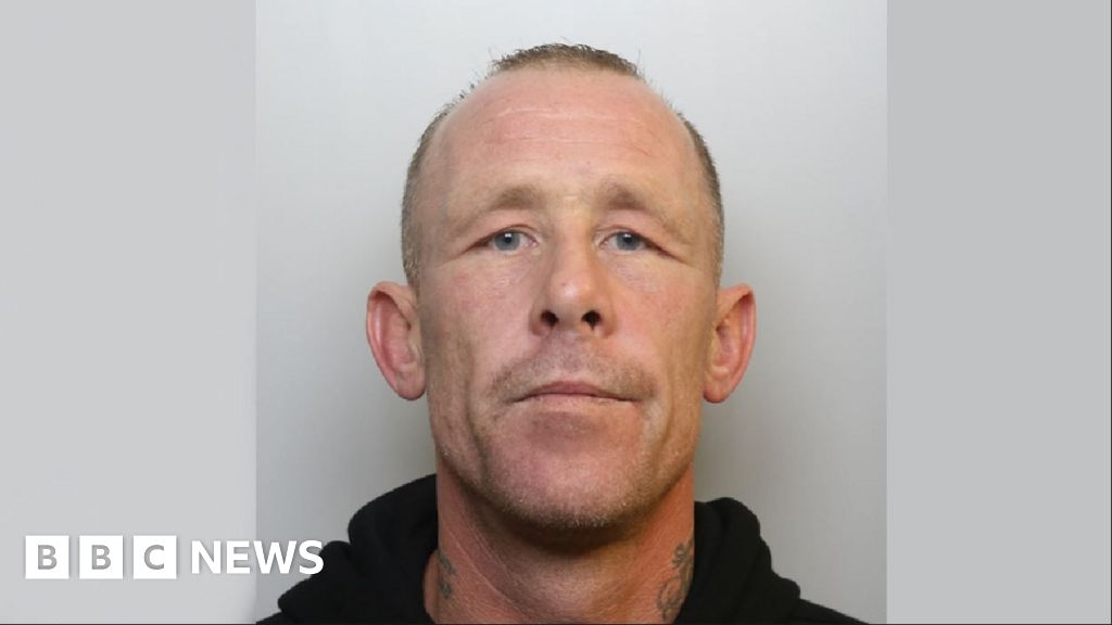 A mugshot of Timbrell ,wearing a black hoodie. He has short hair and a shaven face, with neck tattoos on both sides.