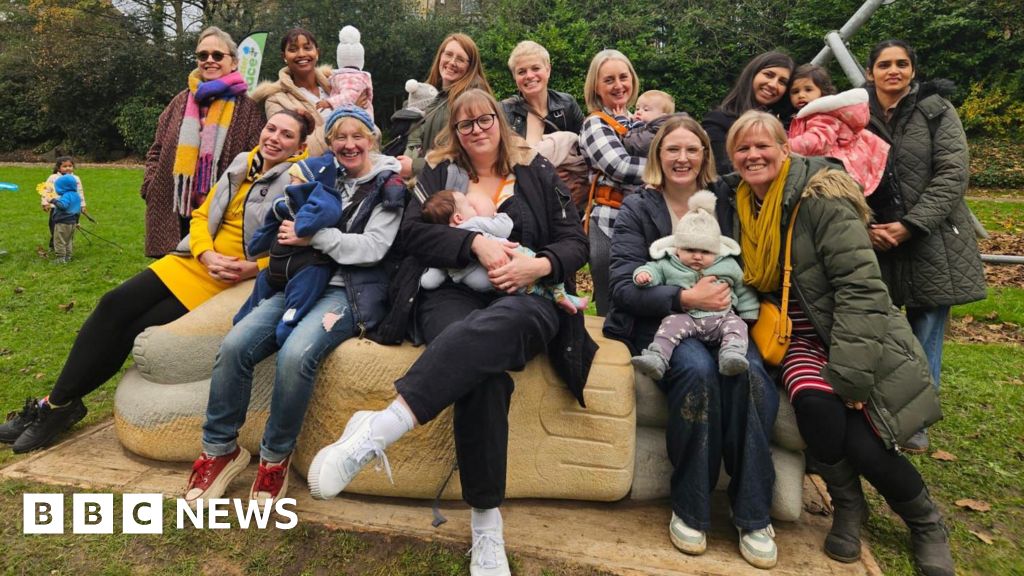 A group of women, some holding babies, sitting on a stone sculpture in a park
