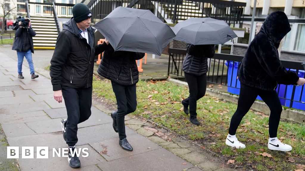 Image of Sophie Harvey and Elliot Benham outside Gloucester Crown Court. They are pictured under black umbrellas concealing their faces. 