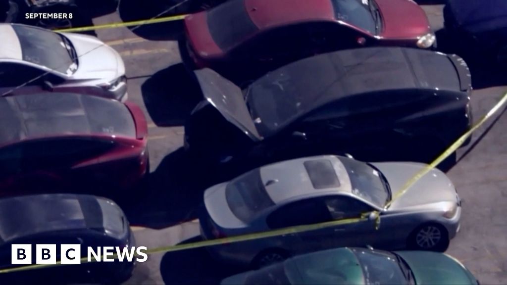 A parking lot with cars, including a black Tesla with the trunk popped open
