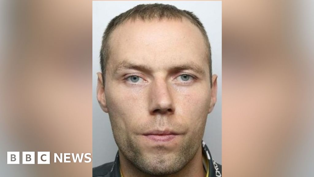 The mugshot of a man who looks at the camera. He has blue eyes and blond hair.