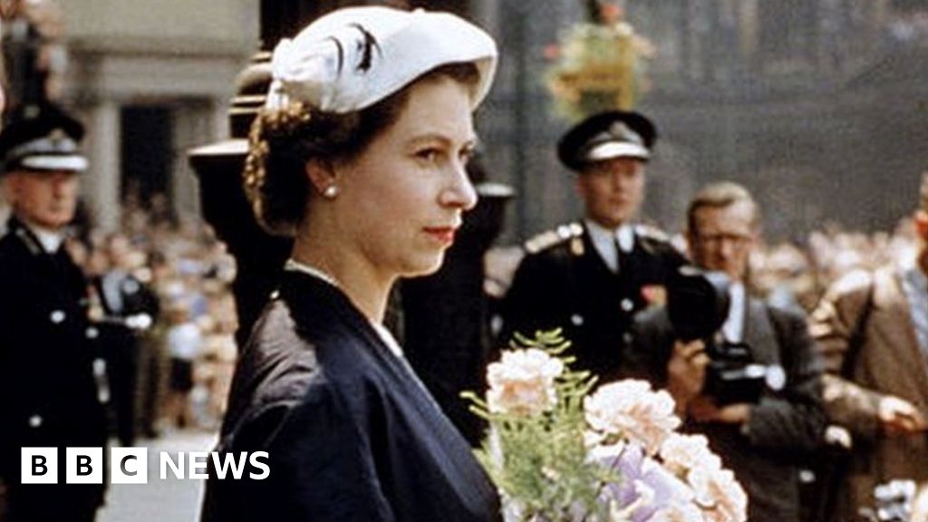 Queen Elizabeth II standing on a red carpet with a posy of flowers