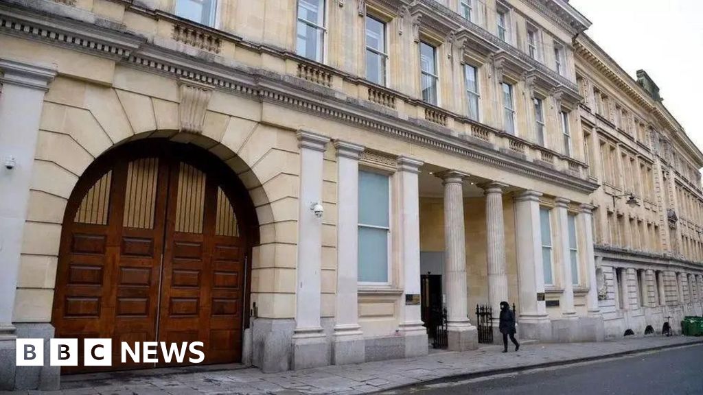 The exterior entrance of Bristol Crown Court. It is a large sand coloured building with white columns outside the front, and large arched wooden double doors on the left.