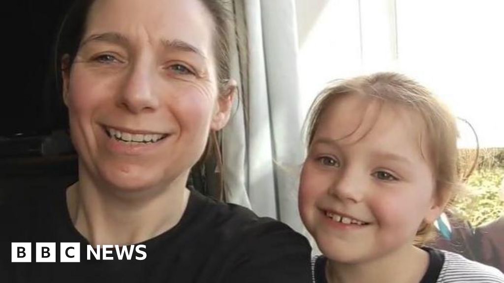 A woman in a black shirt sits next to a small girl in a striped T shirt. They are both smiling at the camera