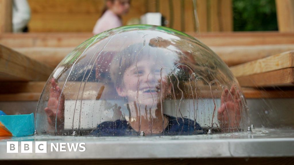 Photo: BBC A boy pokes his head up in a glass lid, which has water dripping down the outside