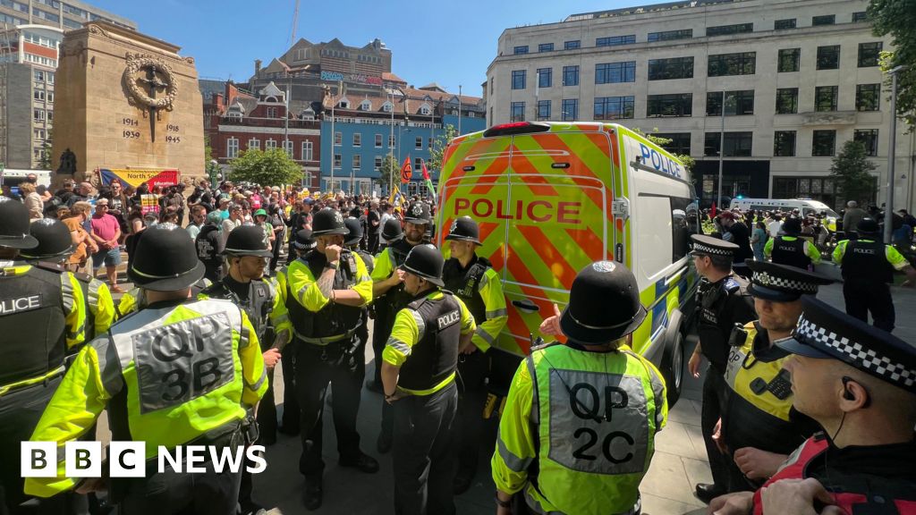 A large group of police stand in front of a van, with lots of protesters in front of the Cenotaph. People can be seen holding banners and flags. 