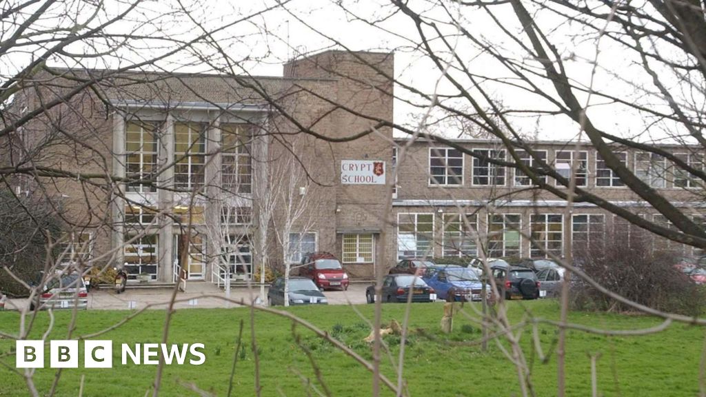 Wide shot of the outside of The Crypt School in Gloucester showing the front of the school, cars in the car park and a lawn.