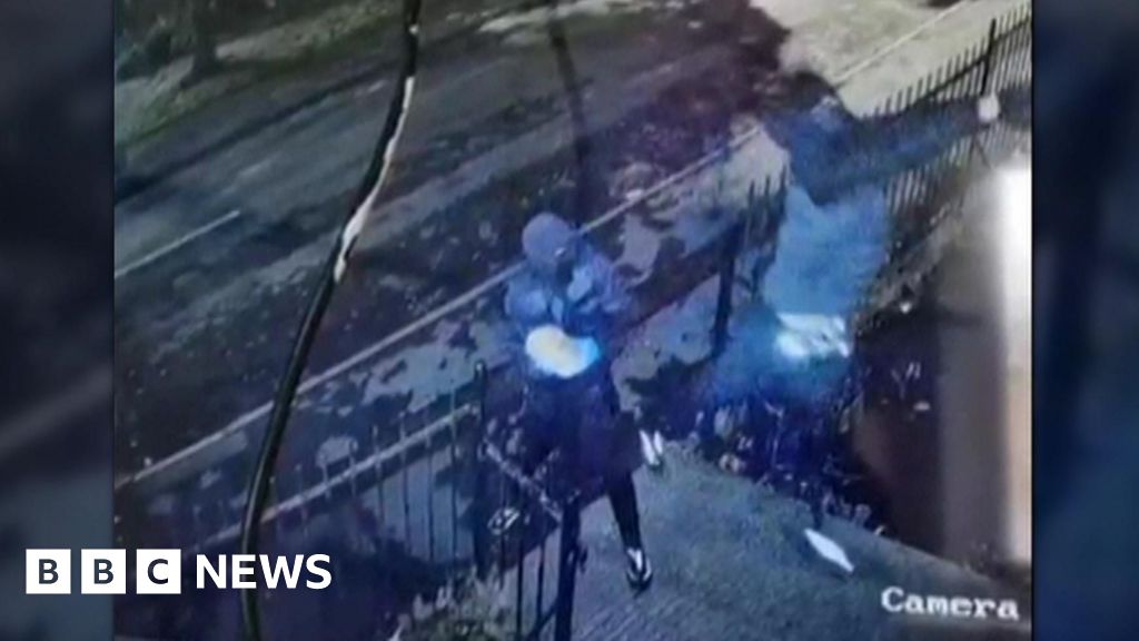 Two people in dark clothing, masks and gloves hold paving slabs - one is reaching up and throwing one