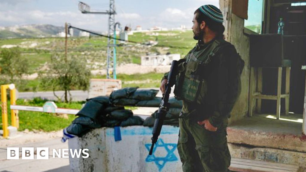 Man wearing kippah stands with gun at checkpoint at an illegal settlement