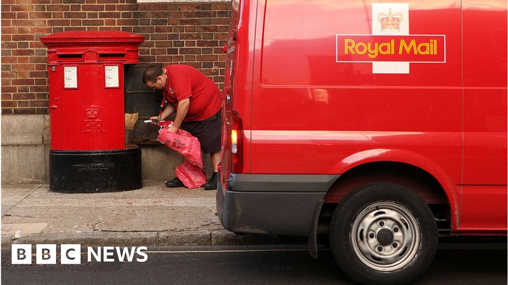Royal Mail worker kneeling behind a Royal Mail red van getting post out of a red post box