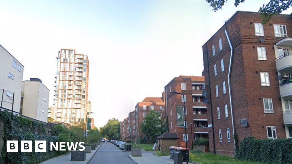 A small residential road is pictured going through Woodberry Down Estate which has several five-floored flats running down the righthand side of the picture and a tower block in the distance on the left