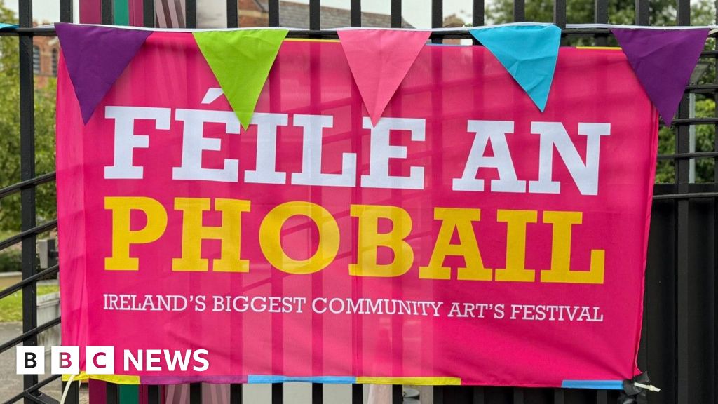 A pink poster with white and yellow writing which says Féile an Phobail on it against black railings