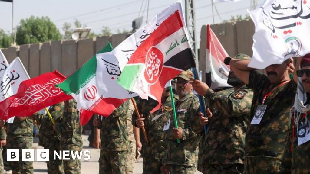Iranian military personnel stand in a line waving red, white, green and black flags.