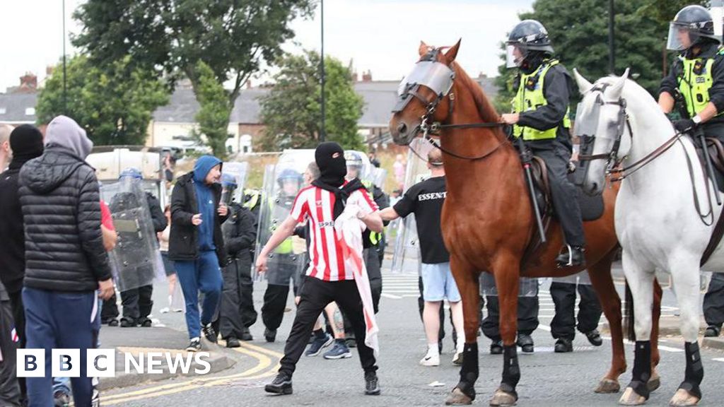 Man in balaclava stares as police officers on horses