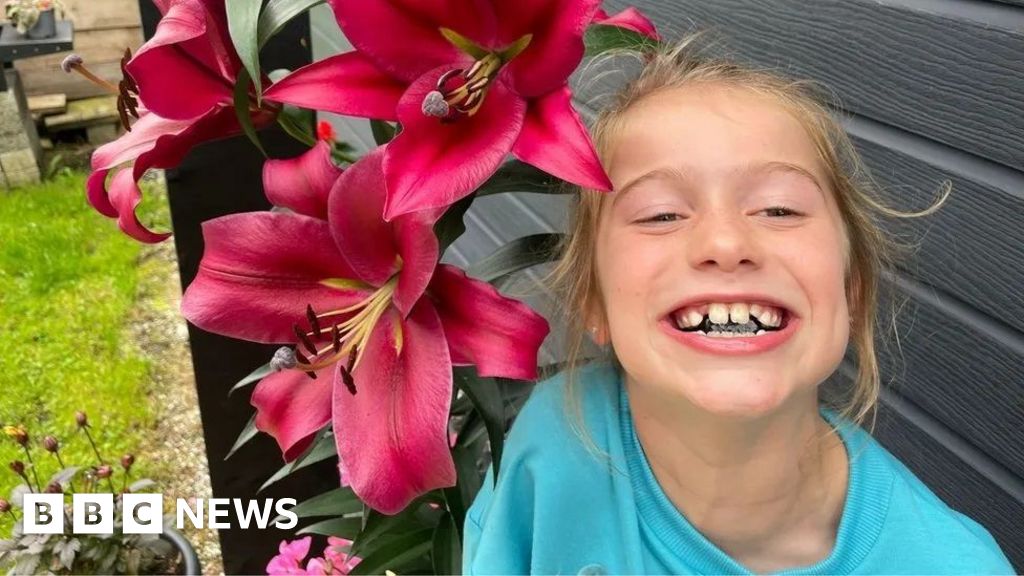 Scarlett Rossborough smiling beside large pink lily